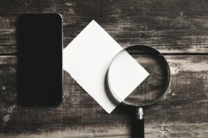 Close-up of a smartphone, a blank piece of paper, and a magnifying glass on a rustic wooden surface, symbolizing digital forensic analysis.